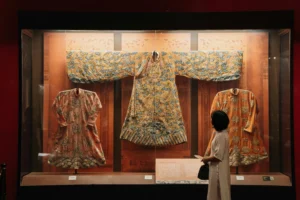 Abiti storici esposti in museo osservati da una visitatrice, rappresentazione del patrimonio tessile e degli archivi della moda