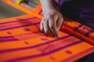 Mano al lavoro su un tessuto realizzato artigianalmente, simbolo della produzione manuale e dell’artigianato contemporaneo nel settore moda.